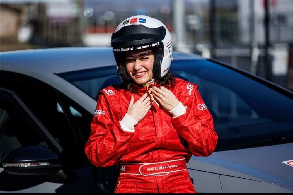 Isabel Díaz Ayuso con un mono de carreras rojo abrochándose un casco de carreras rojo.