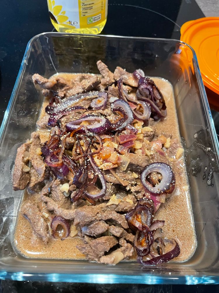 A glass dish of Bistek Tagalog, a Filipino dish of beef sauteed with onions, garlic, soy sauce and black pepper