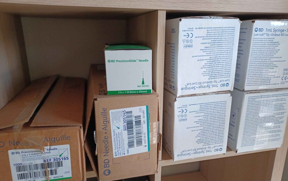 cardboard boxes on a shelf. the boxes contain 400 BD syringes and 1000 needles of two different gauges 