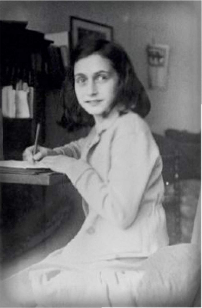 Black and white photo of holocaust victim Anne Frank seem sitting, writing at a desk