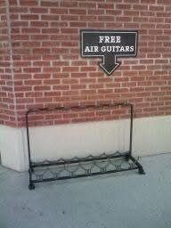 Guitar rack filled with air guitars or an empty rack containing nothing but the black sign above says free air guitars 
