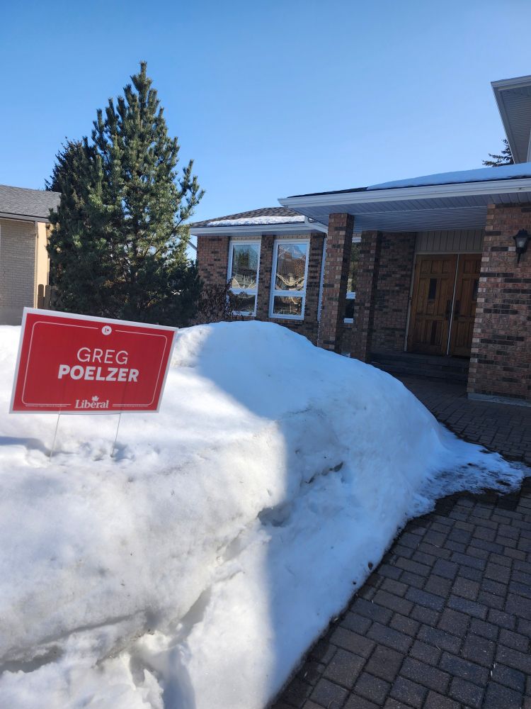 Red Liberal sign for Saskatoon University candidate Greg Poelzer, on top of snowbank in front of our house.