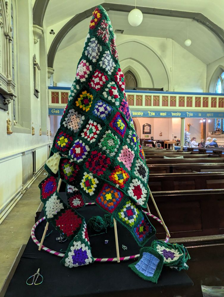 A partly assembled Christmas tree made up of crochet granny squares inside a church 