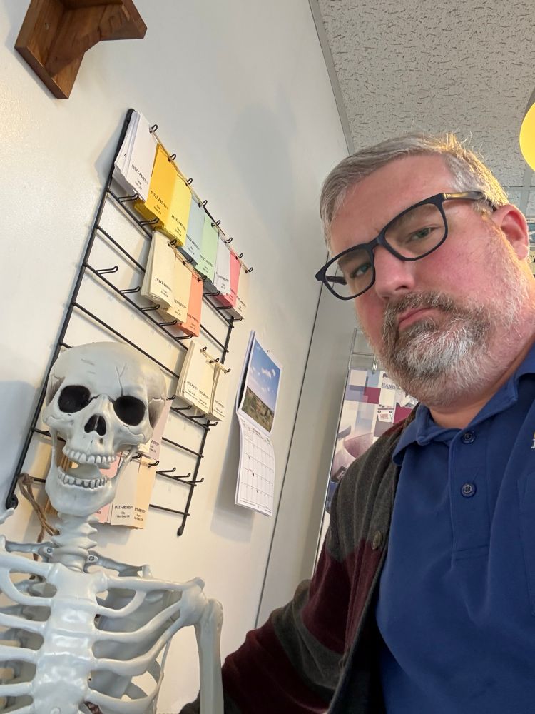 Man standing to the right of a plastic skeleton 