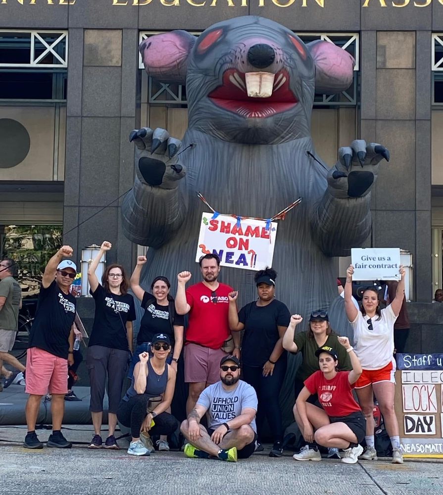 2024 NEA Lock out of staff. Digital Team posing stoically in front of scabby the rat. 