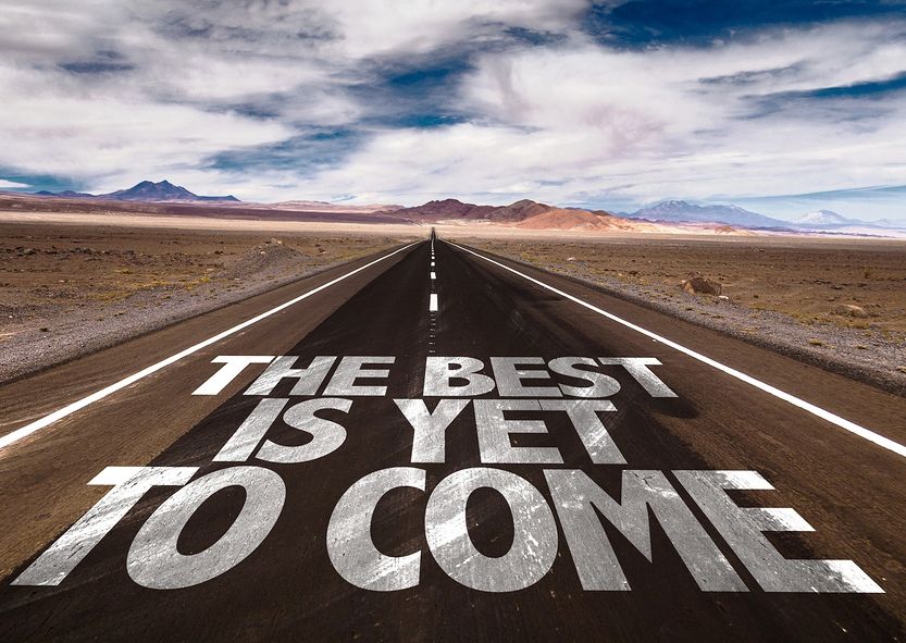 Open road through desert with text "THE BEST IS YET TO COME" on asphalt. Mountains in background, sky with clouds. Optimistic mood denoting a positive outlook for spinal decompression therapy in Cary, NC