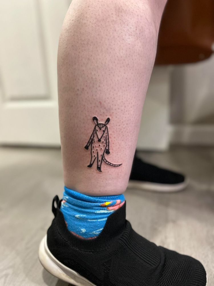 A photograph of a freshly completely tattoo on Fofo's lower leg. It's a lineart doodle of a possum standing on his hind legs. 
