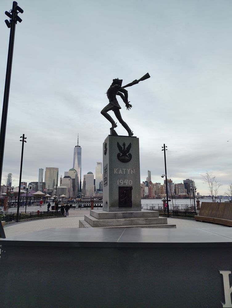 A statue of a man getting stabbed in the back by a bayonet. The stone base reads "Katyn 1940".