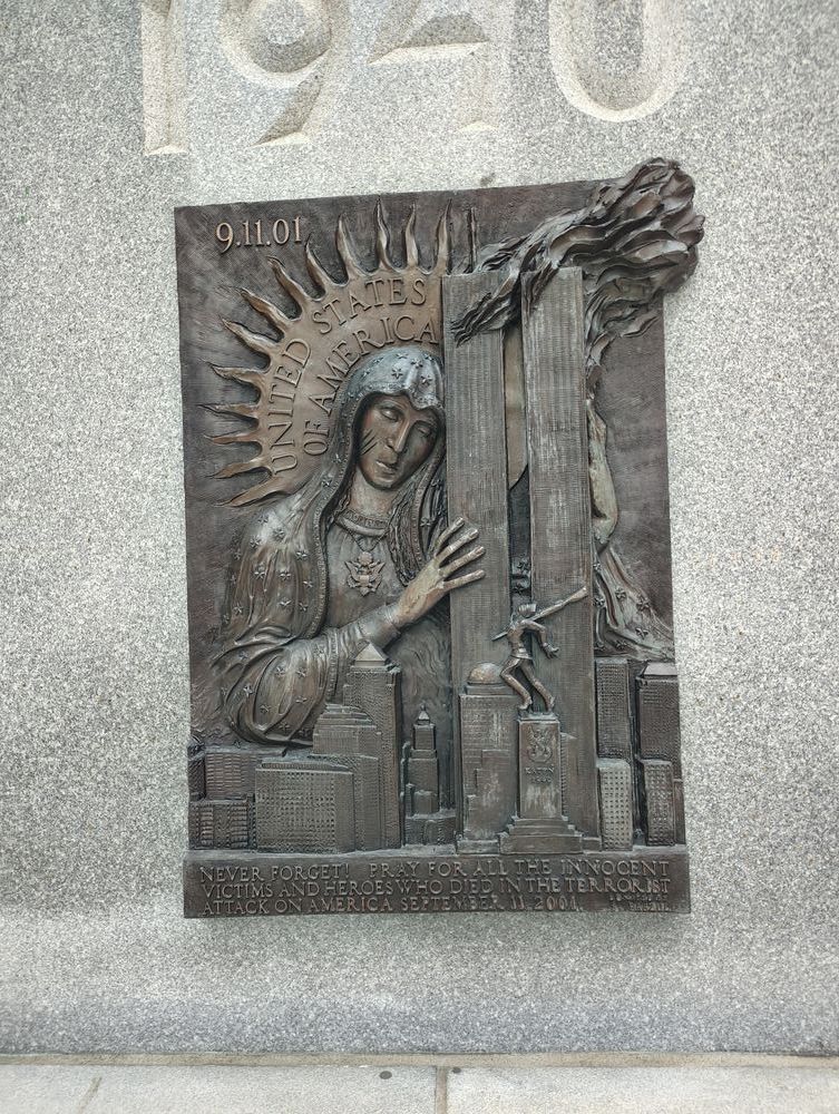 A metal bas relief of the Twin Towers with the aforementioned statue depicted in front. The Towers are being embraced by a giant Jesus.