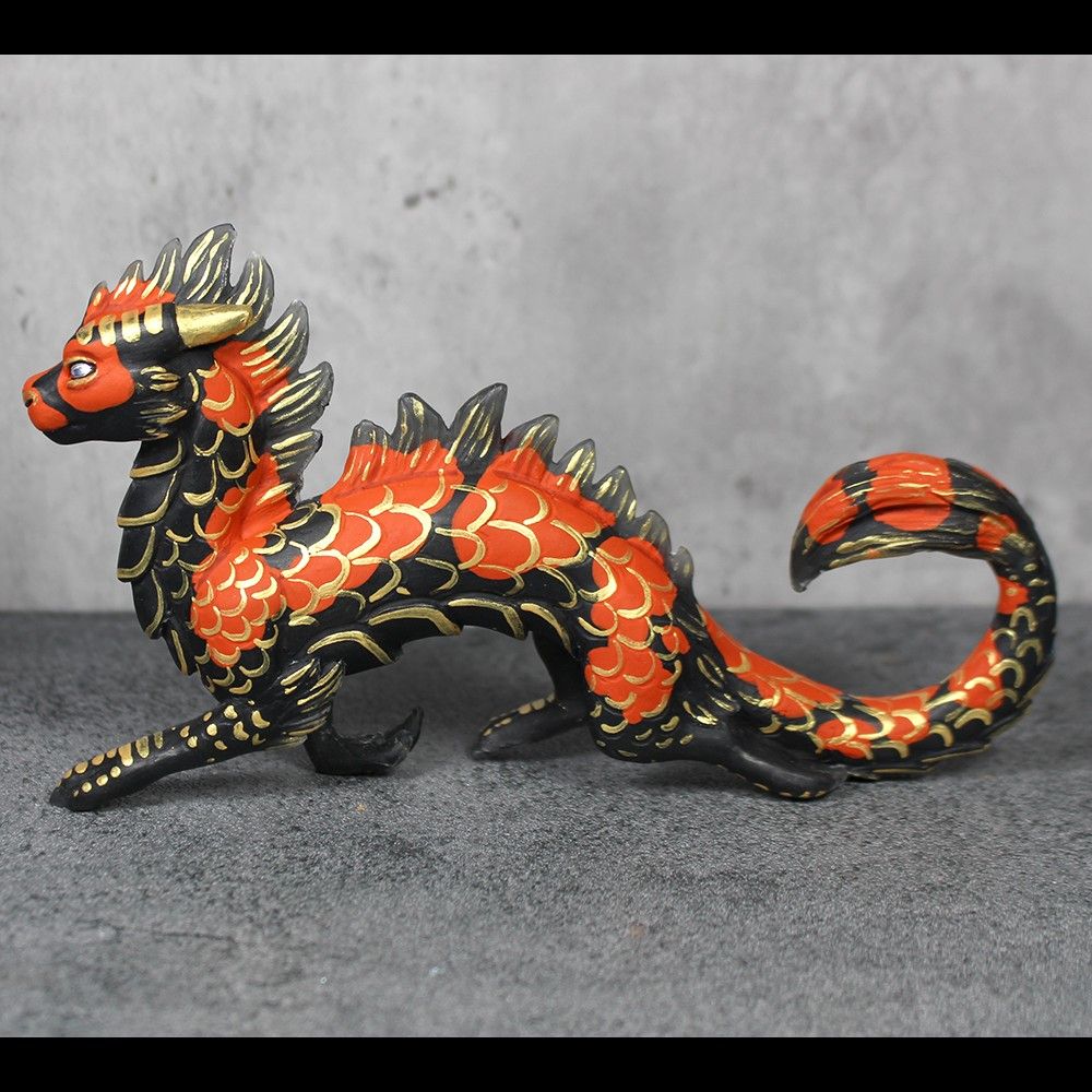 A sculpture of an eastern style dragon, painted like a koi fish.  He is prancing jauntily.  He is black with orange spots, accented with metallic gold scales.