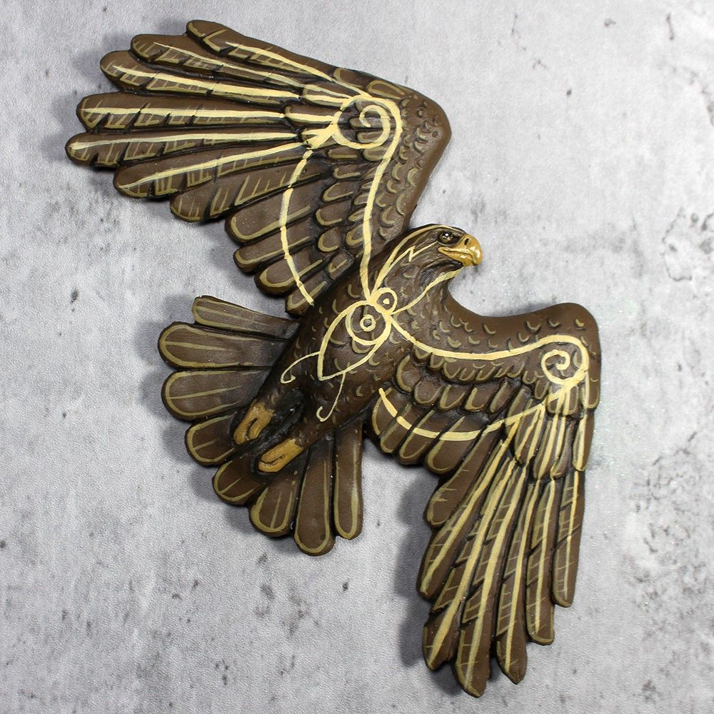 A flat magnet sculpture of a golden eagle in flight, seen from below.  He has swirly yellow markings all over.