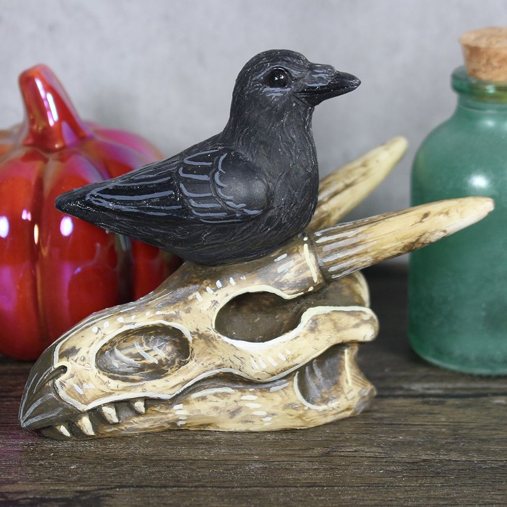 A sculpture featuring a crow sitting on a dragon skull.
