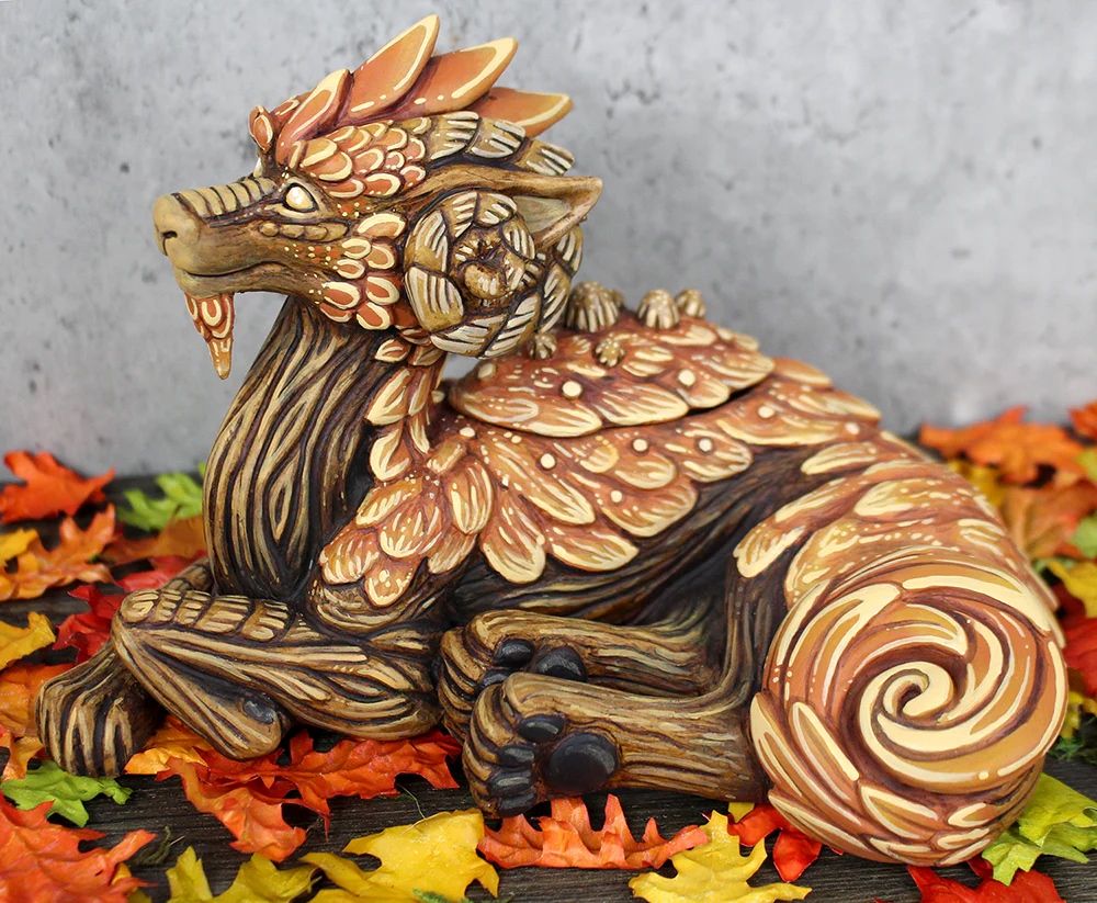 A large reclining tree dragon sculpture.  Its skin is made of brown tree back and it's back is covered in orange moss.  There are leaves on the head and tail tip.