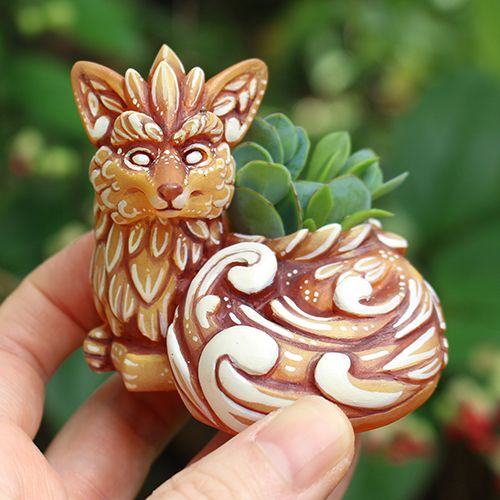 A photo of a figural fox mini planter with a small succulent. The fox is orange and embellished with swirls and leaves. 