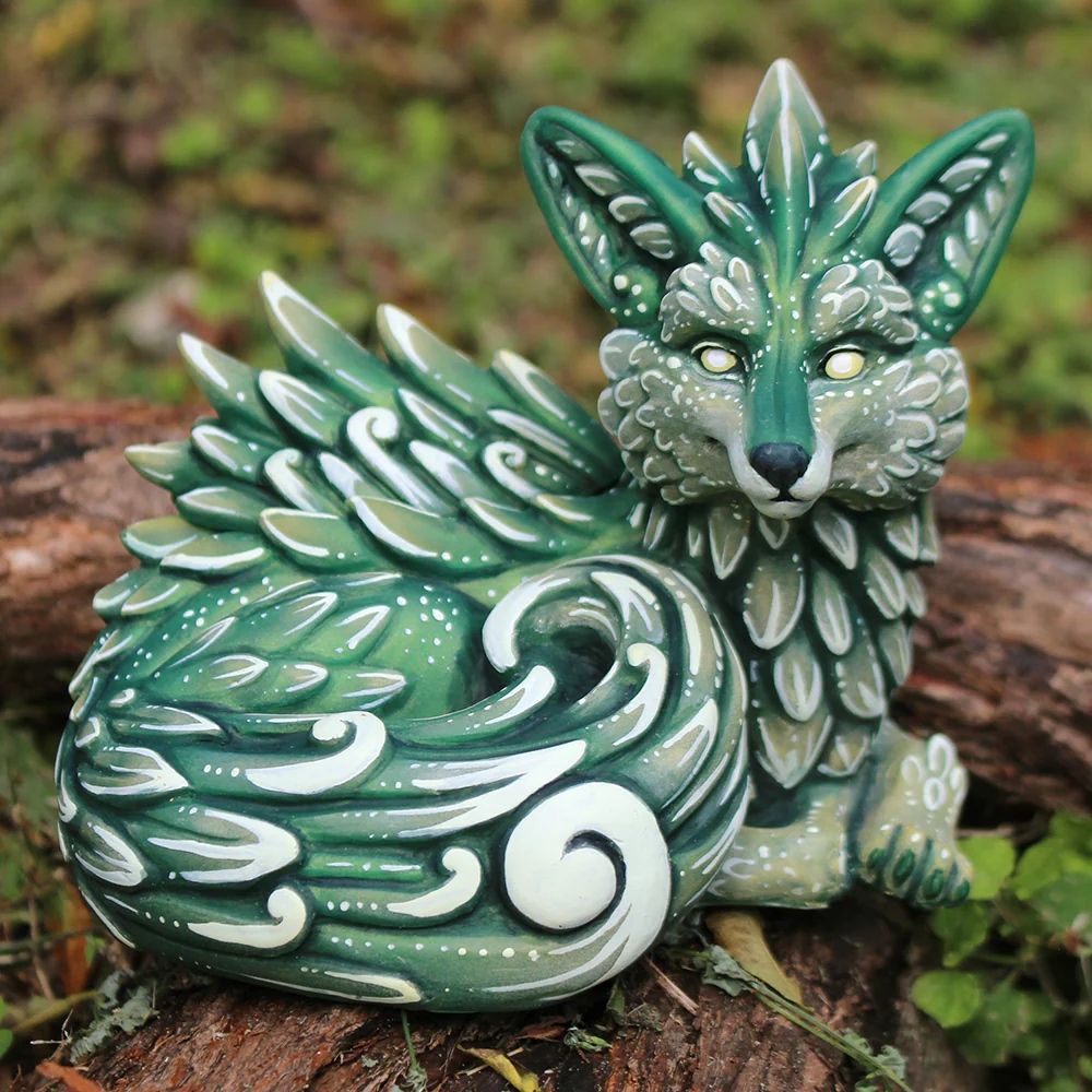 A photo of a green fox sculpture sitting on a branch. He is covered in leaves and swirls. 