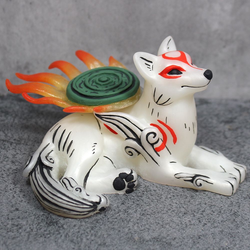A photo of a figure of the white wolf Amaterasu.  She is lying down and looking up, her flaming shield upon her back.