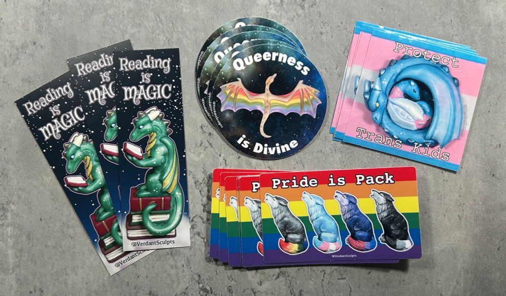 A photo of a selection of stickers and bookmarks on my desk, most featuring dragons. 