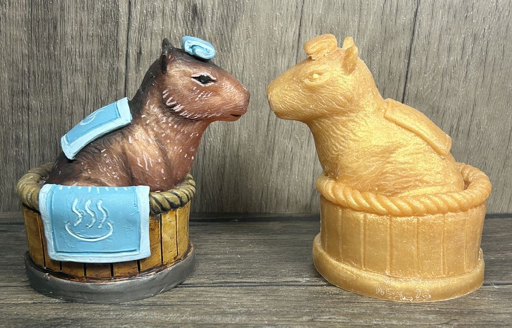 A pair of figures featuring a capybara seated in a spa tub.  Towels are draped over the side of the tub and along the capy’s back.  A folded towel rests on it’s forehead.