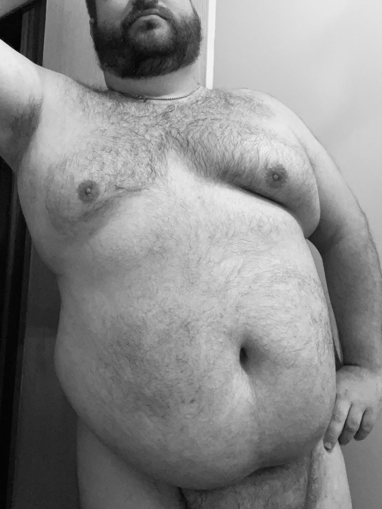 Black and white photo primarily of my chest and yummy. Right arm leaning against the wall and left hand on my hip. Cropped right above my mouth and above my pubes