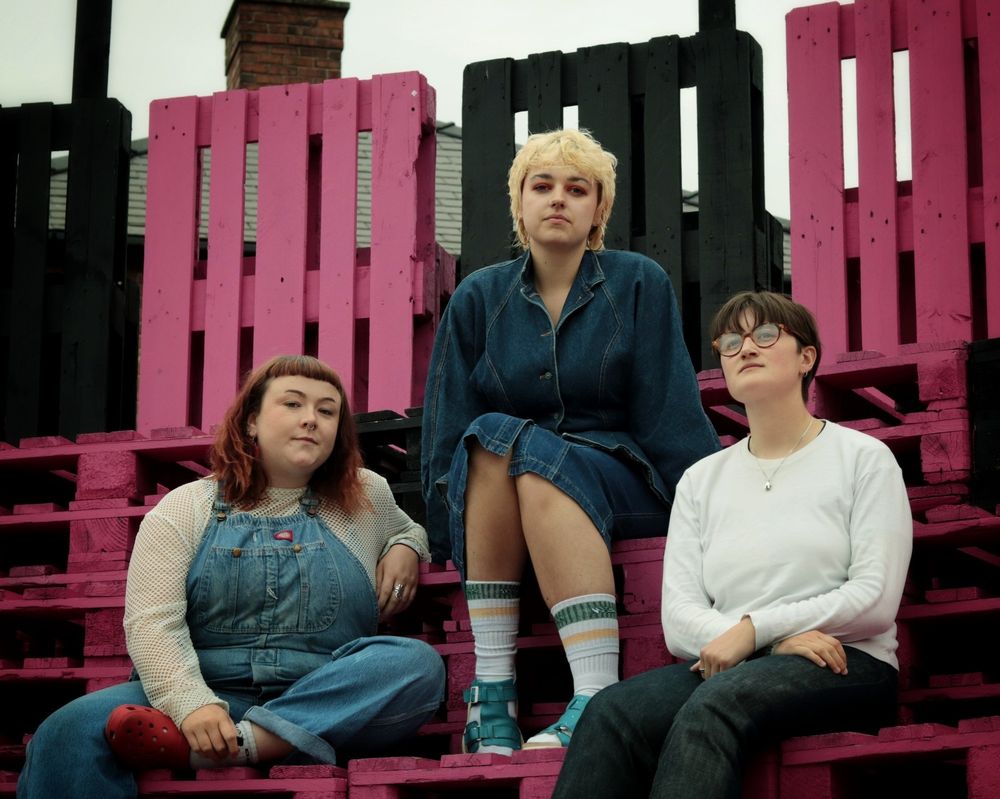 The band Adwaith sitting on pink and black decking made from pallets