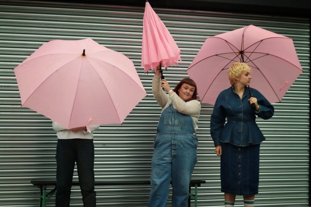 The band Adwaith standing holding pink umbrellas