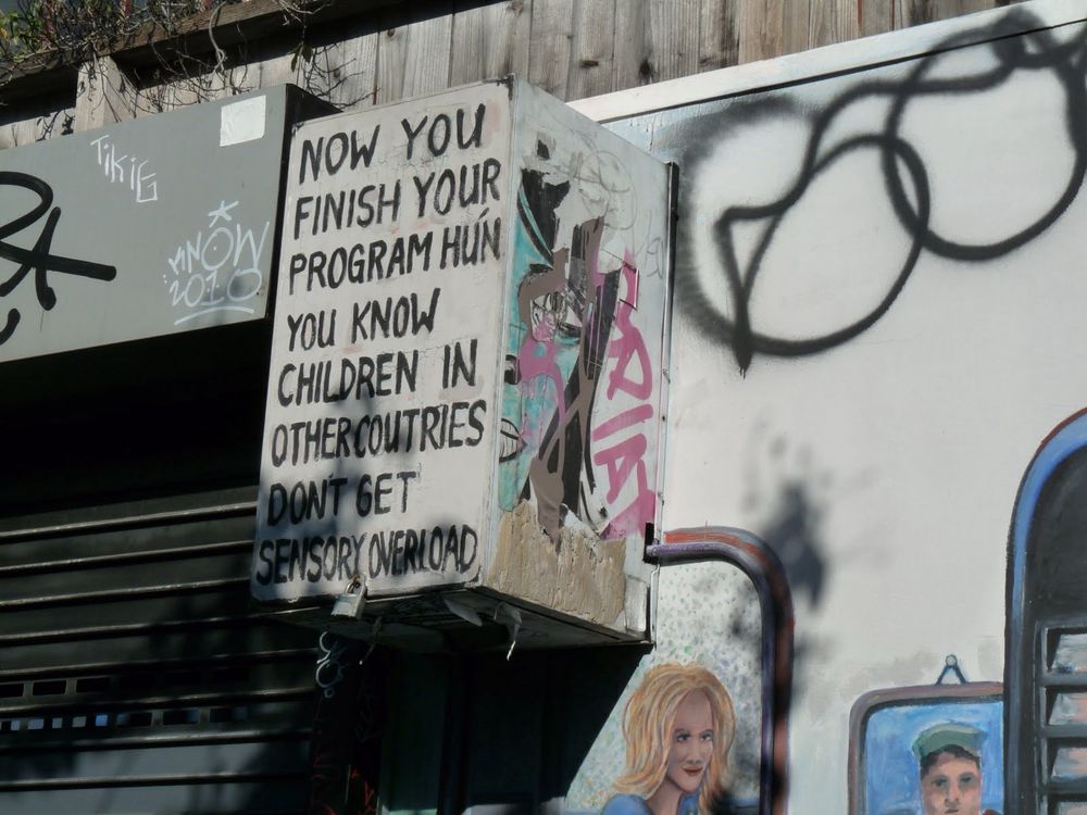 Art in an alleyway that reads: NOW YOU FINISH YOUR PROGRAM HUN YOU KNOW CHILDREN IN OTHER COUNTRIES DON'T GET SENSORY OVERLOAD