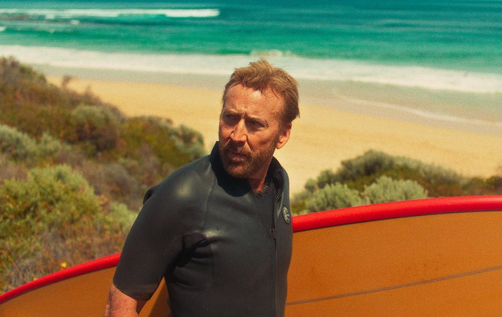 Nicolas Cage holding a surf board in the movie THE SURFER