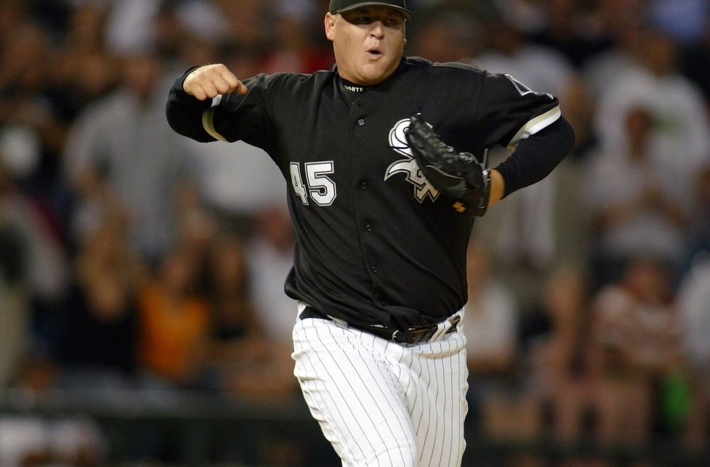 Bobby Jenks, a large white man, in a Chicago White Sox uniform, black jersey, white pants with black pinstripes, looks like he's leaving the mound celebrating an out.