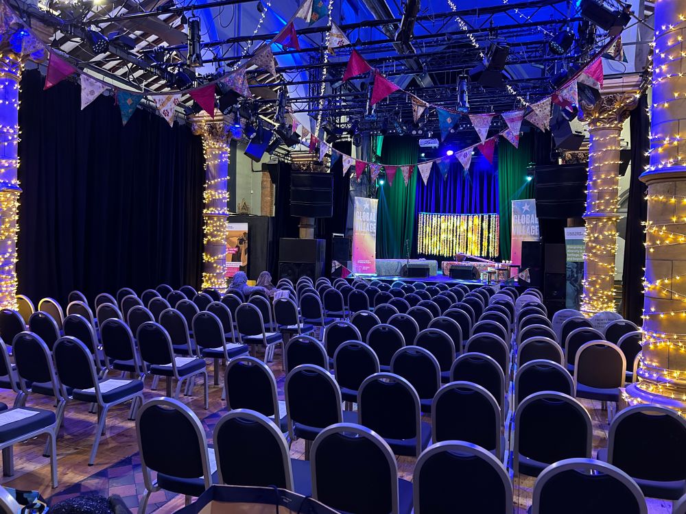 A photo taken inside a Colchester Arts Centre, a converted church into an arts centre. Photo shows the set up for a seated gig with chairs in rows and a lit raised stage. 