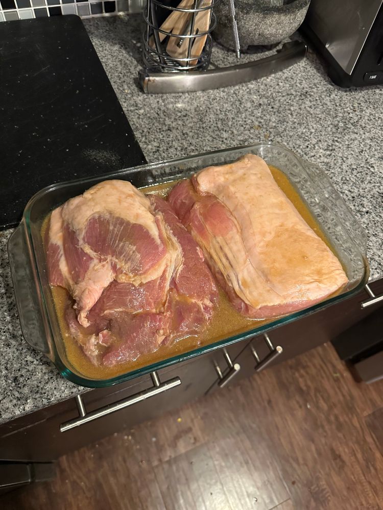 A Pyrex baking dish full to the brim with two massive halves of a raw pork roast with marinade.
