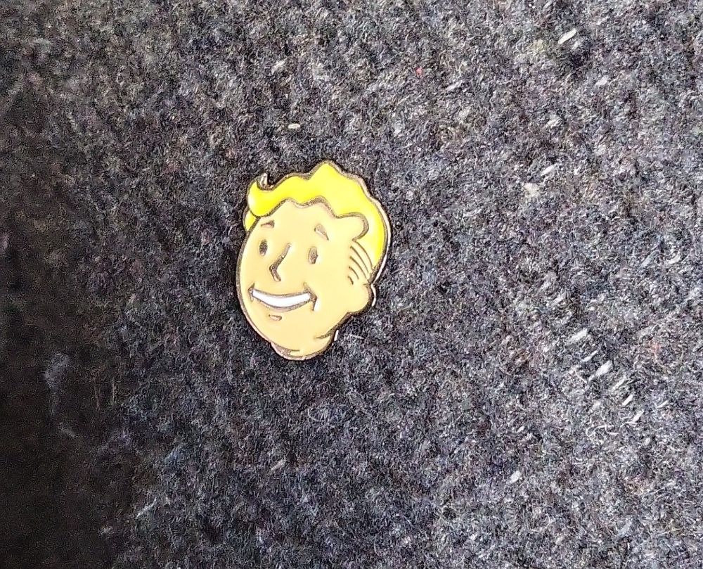 Vault tech mascot head image on metal pin, like the face on the bobbleheads in-game.