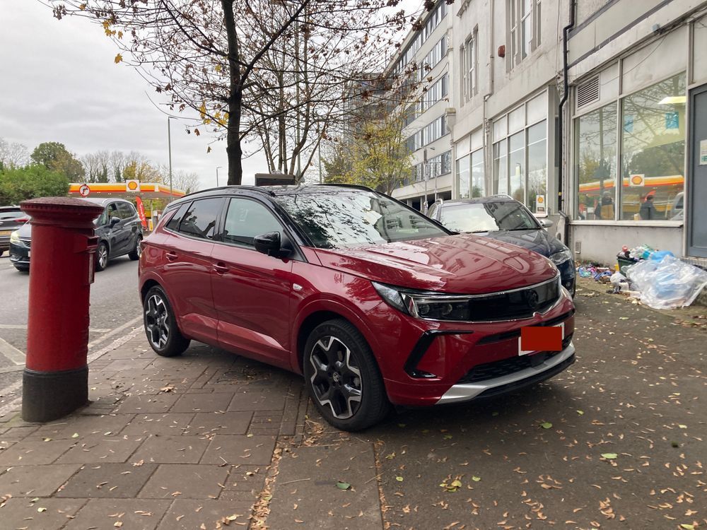 A large car is parked on a pavement, completely obscuring it for pedestrians. 