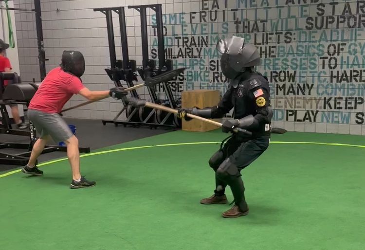 Two people in fencing masks fighting with rubber training spears. 