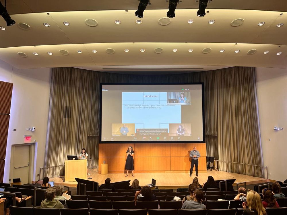 Serpil (presenter) is on the left on the stage, presenting the results. Two interpreters are on the stage, IS interpreter in the middle, ASL interpreter on the right.