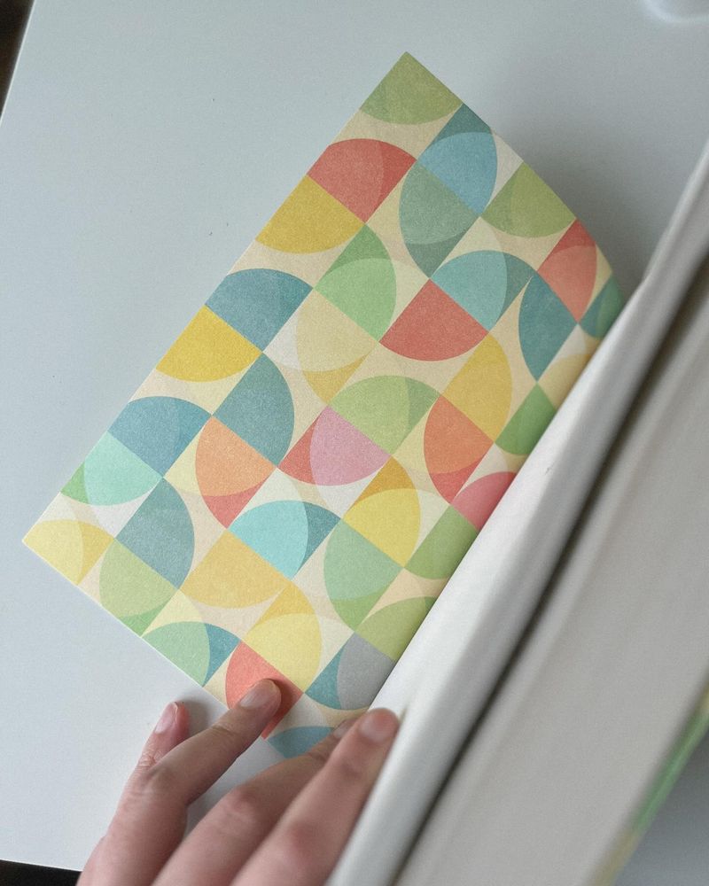 The Fun Times Brigade on a white desk with my hand opening the book to show the colourful blue, green, orange, and yellow endpaper.
