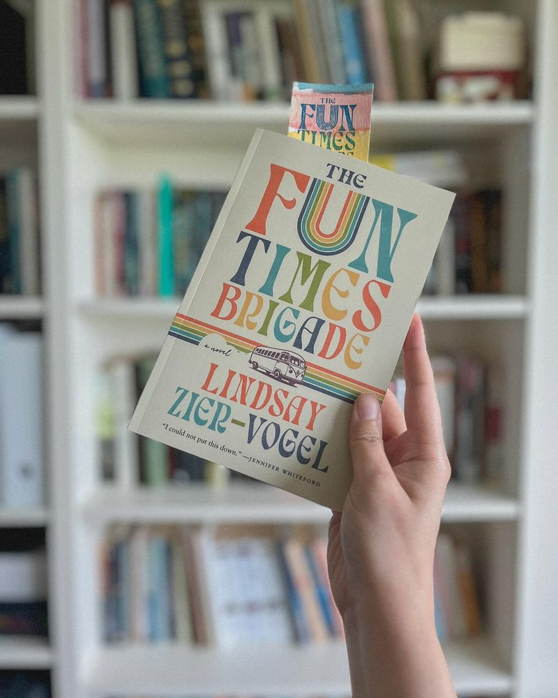 My hand holding a copy of Lindsay Zier-Vogel’s The Fun Times Brigade against a white bookcase