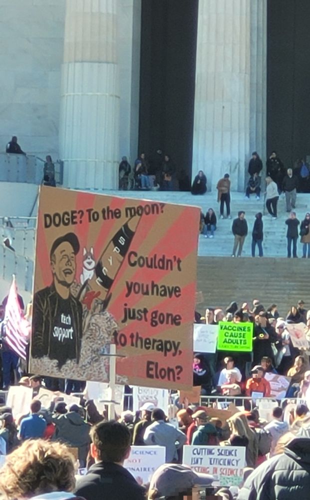 Sign includes a pic of Elon Must wearing a black t-shirt with white lettering "tech support" and to his right, a picture of a rocket with what looks like russian lettering (chuckle) and what I assume is a picture of Laika, a Soviet dog sent to space in 1957, and who was sadly sacrificed in this enterprise. Blech.