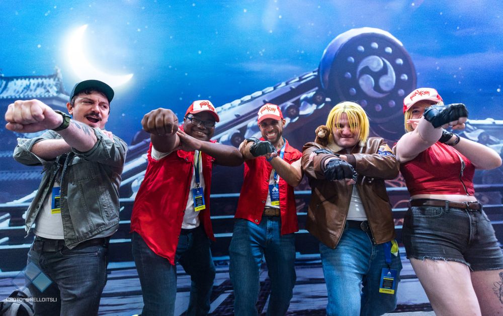 Photo of me at EVO, in front of a backdrop featuring japanese traditional buildings. There are 4 awesome Terry cosplayers with me and we're all standing in a row doing the Buster Wolf pose together.