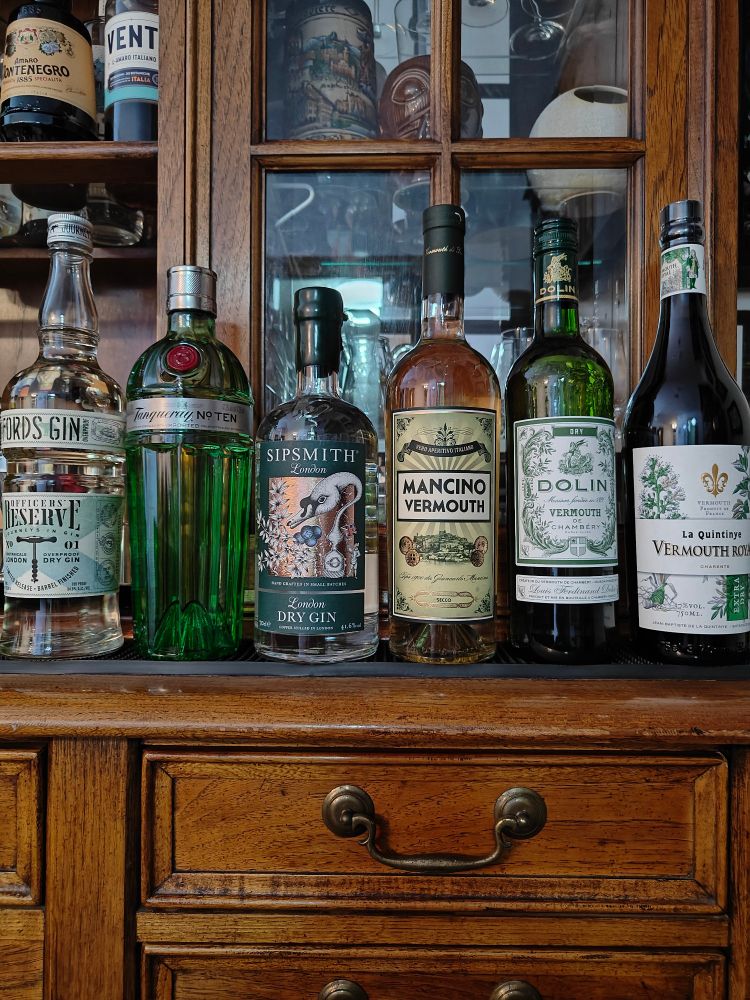 Three bottles of gin and three bottles of dry vermouth on a home bar