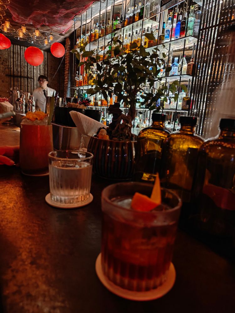 A cocktail glass lit in red lighting on a bar with the back bar visible in the background. 