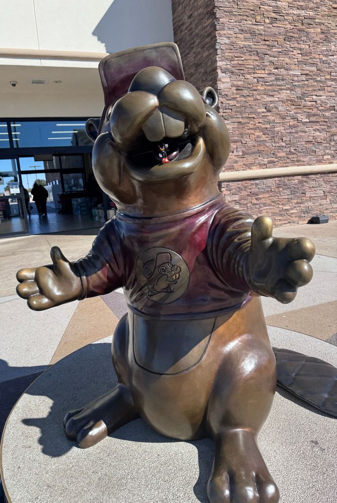 a statue of buc-ee the beaver with a small shadow the hedgehog figurine in his mouth 