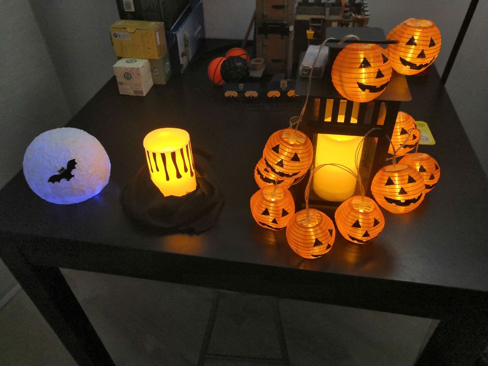 A black table with a hand-crafted moon with a bat on it, a candle with fake dark blood and a lantern with pumpkin-shaped lights scattered over it