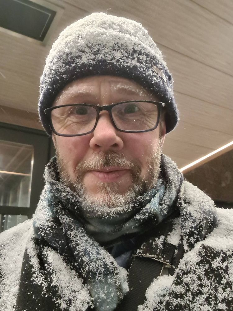 Picture of Jon with shoulders and beanie hat covered in snow. He's still smiling, but weakly