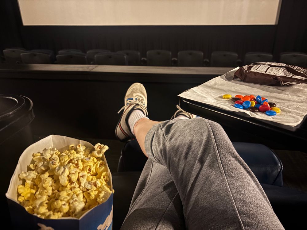 Movie theater seat with popcorn and candy, legs crossed in the theater seat
