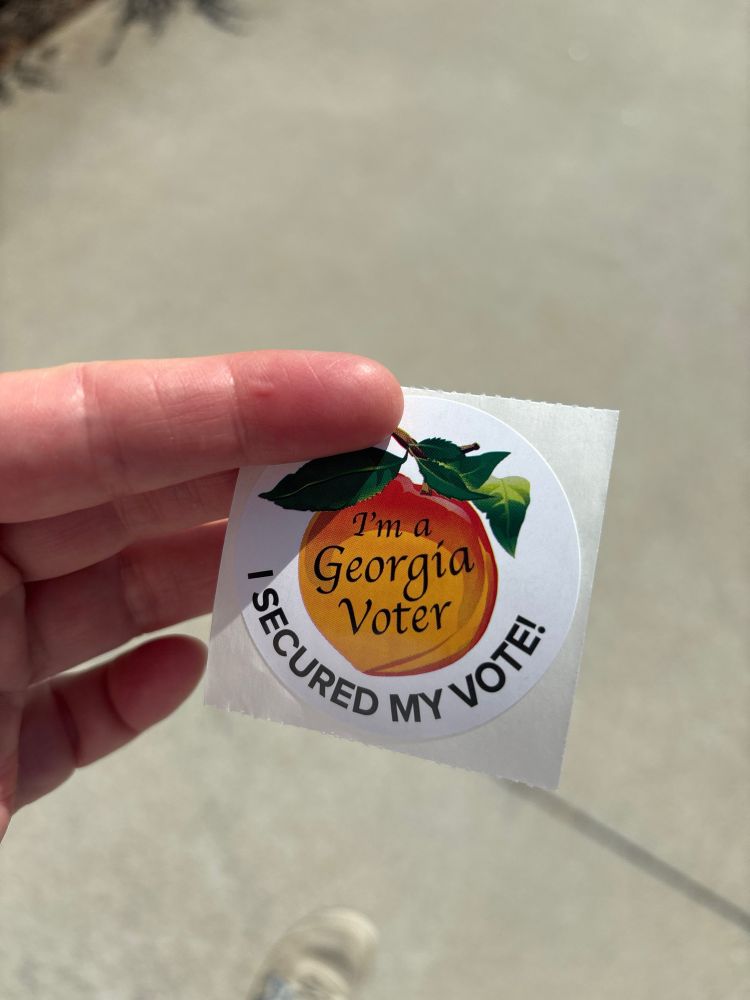 Hand holding a sticker that says “I’m a Georgia voter” in the middle and “I secured my vote” along the outer edge