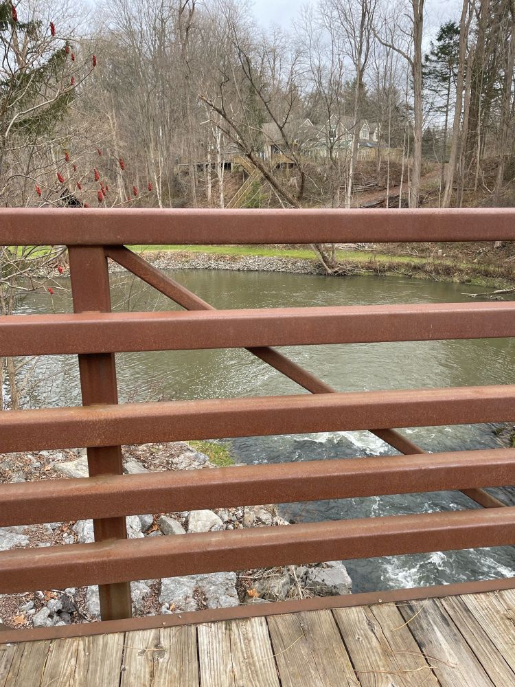 River flows under a wooden and metal bridge. 