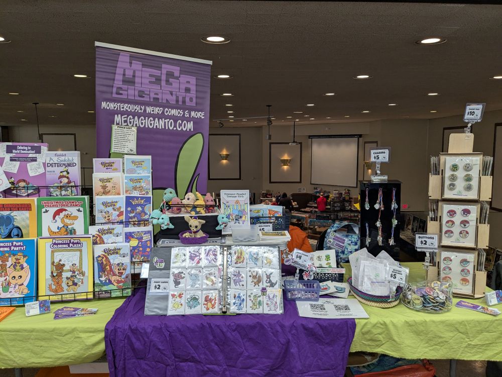 A vending table setup for Lindsay Hornsby featuring her comics, coloring books, prints, crochet and more!