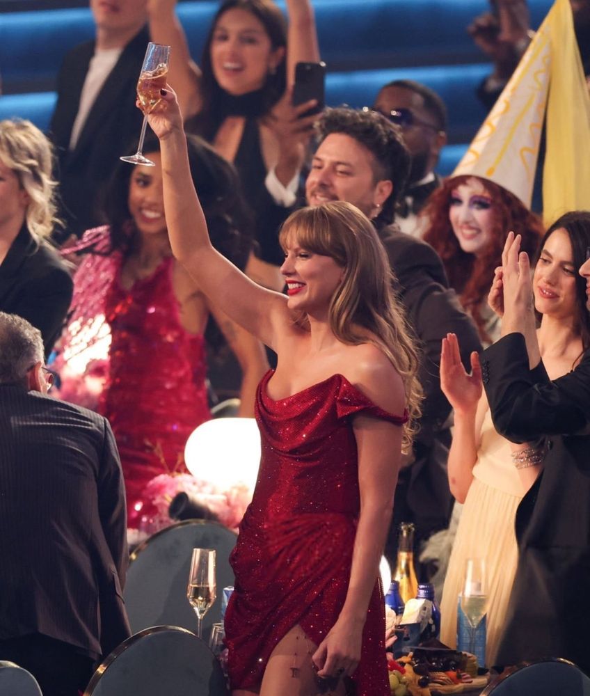 Taylor Swift in her red short Grammys dress, raising her glass to cheer for another artist