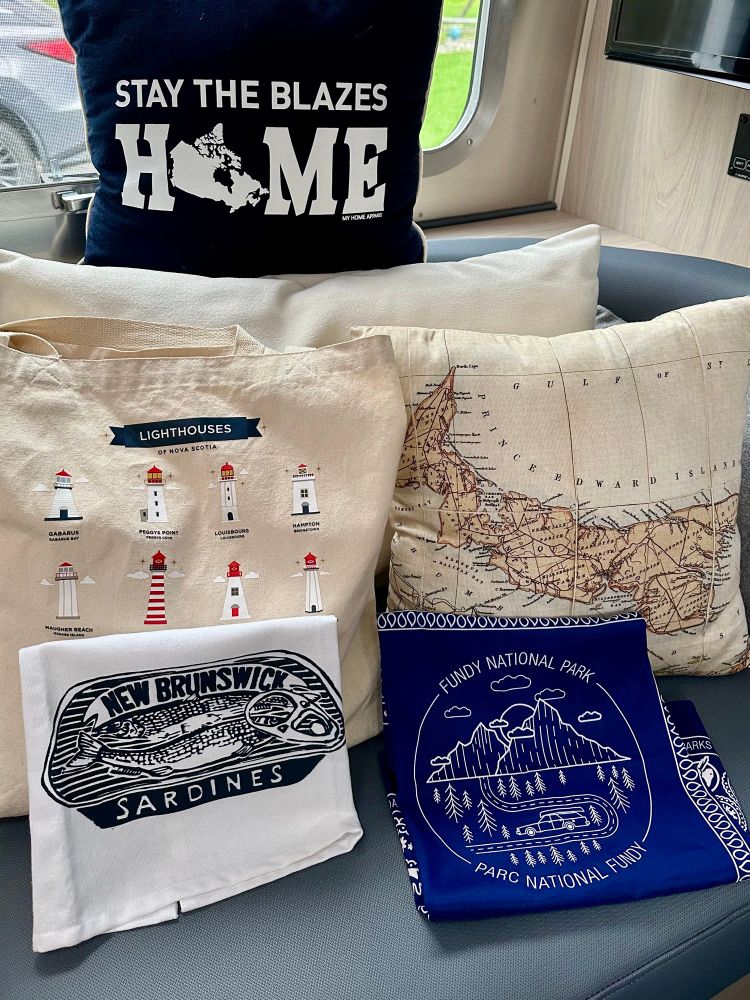 A variety of items from the Maritimes including tea towels from New Brunswick, pillows from PEI and NS, and an NS lighthouses canvas bag. 