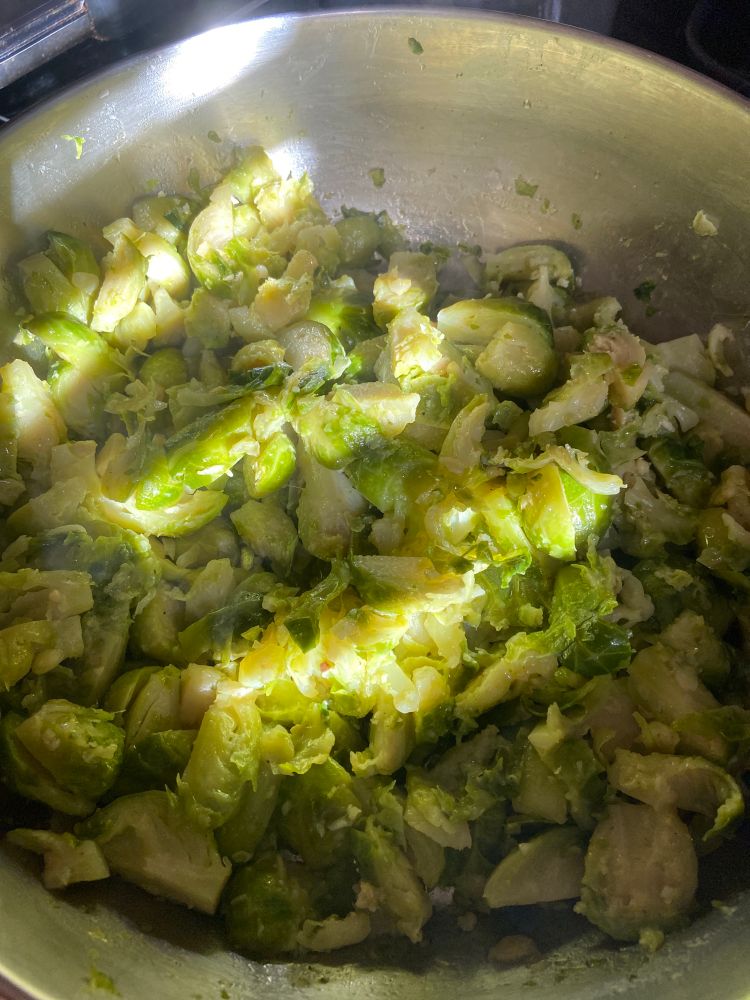 Bright green glazed Brussels sprouts in a silver pan on a black granite stove top. 